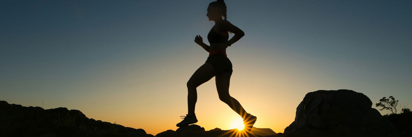 silhouette of man jumping on rocky mountain during sunset